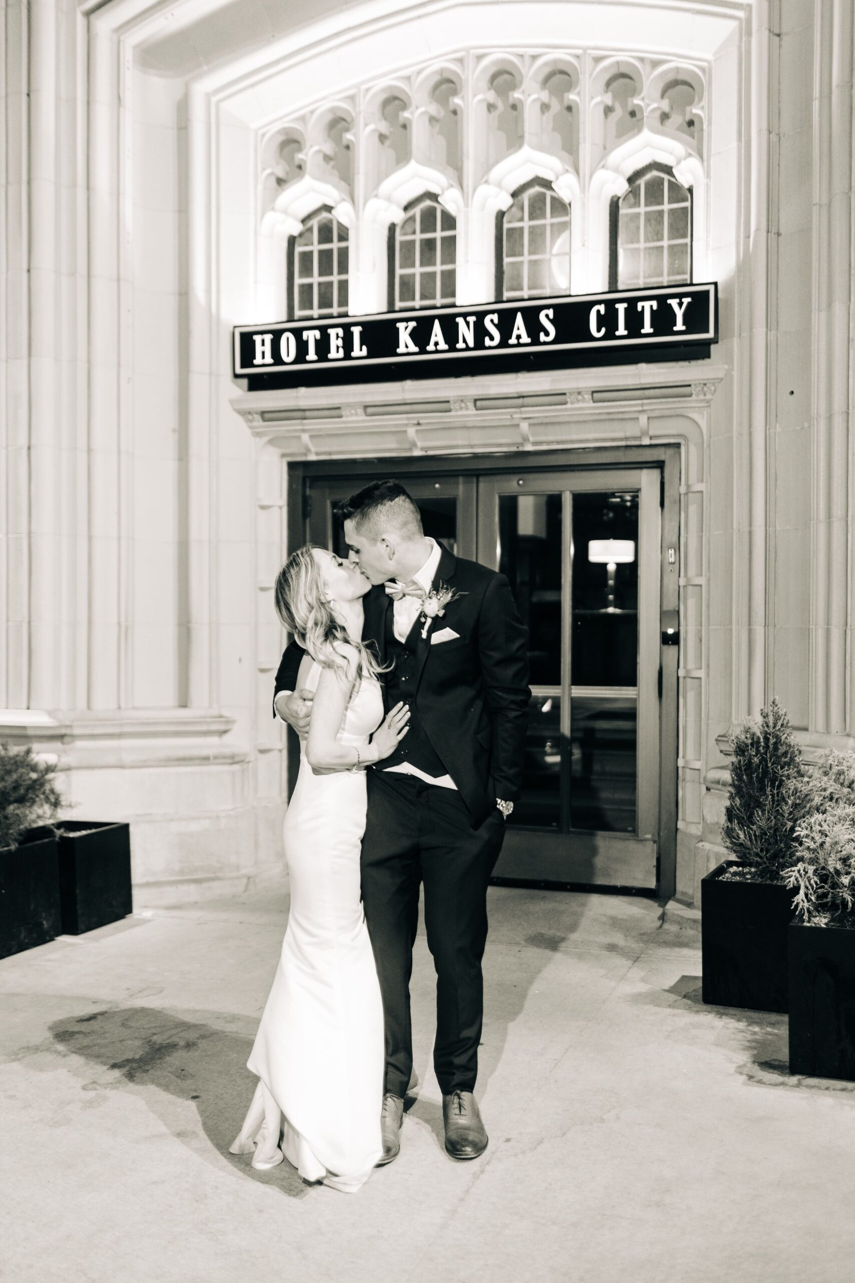 Black and white photo of a bride and groom kissing outside of Hotel Kansas City at the end of their wedding