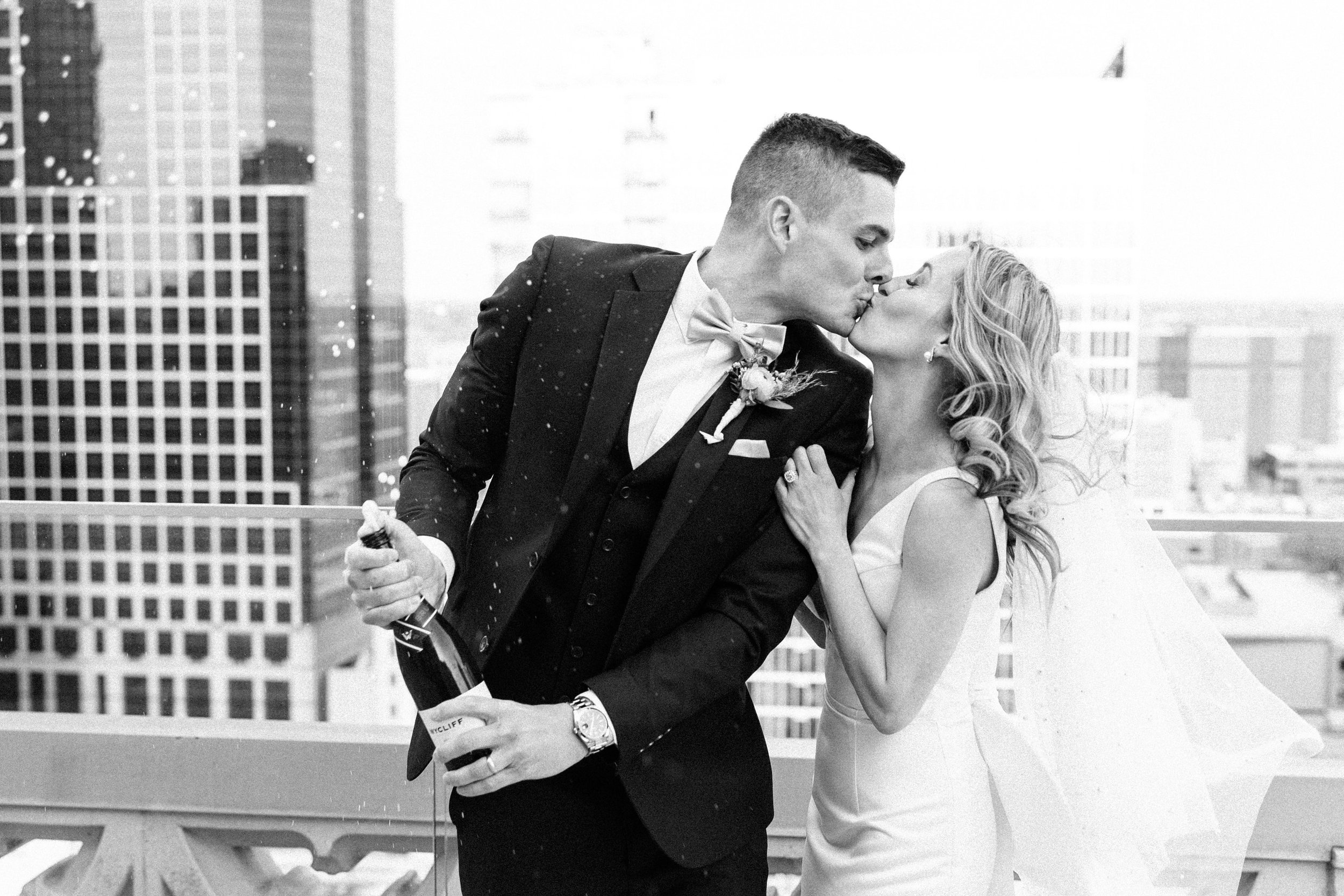 Black and white image of a couple popping champagne on the Starlight Terrace at their Hotel Kansas City wedding