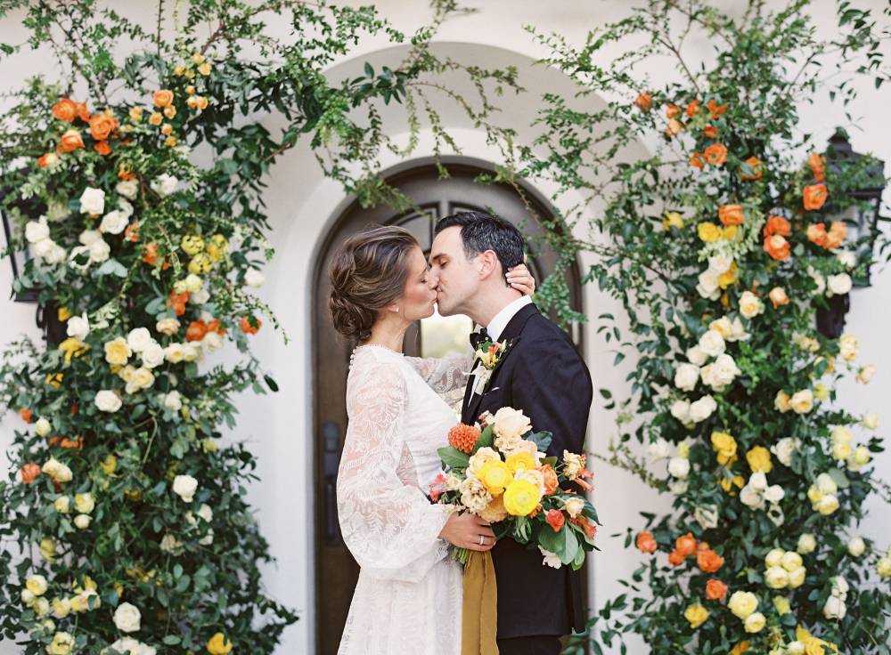 bride and groom kissing in front of a large floral installation