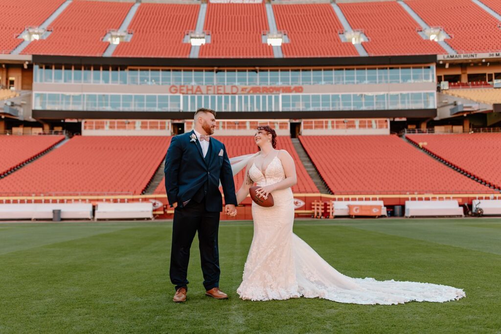 bride carrying football and groom on the field at their arrowhead stadium wedding