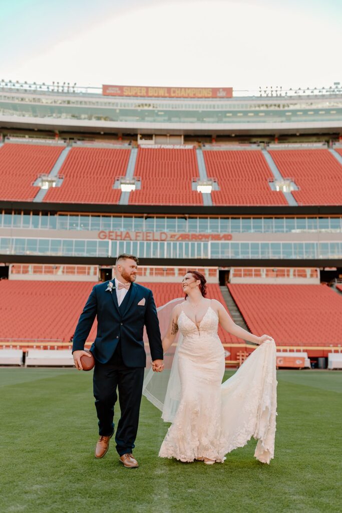 bride and groom carrying football on the field at their arrowhead stadium wedding