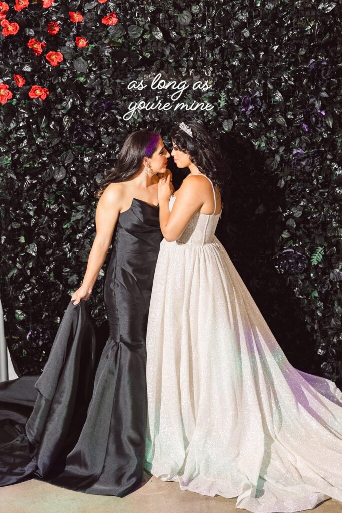 two brides in front of black floral wall