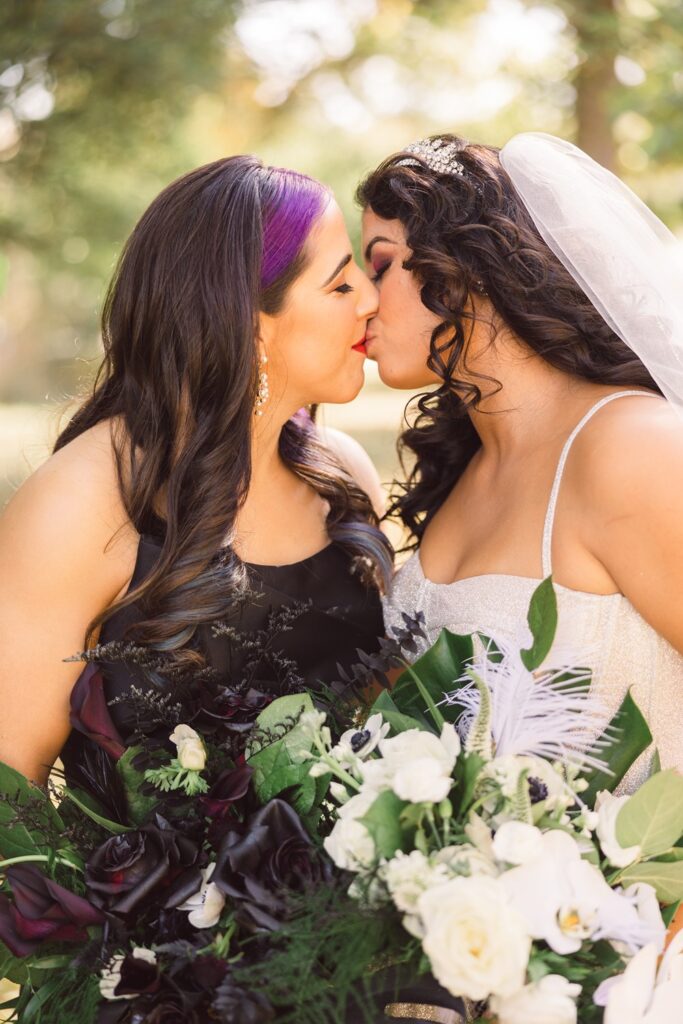 brides kissing while holding their black and white bridal bouquets