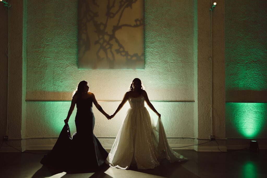 two brides in black and white wedding dresses in front of green and amber uplighting