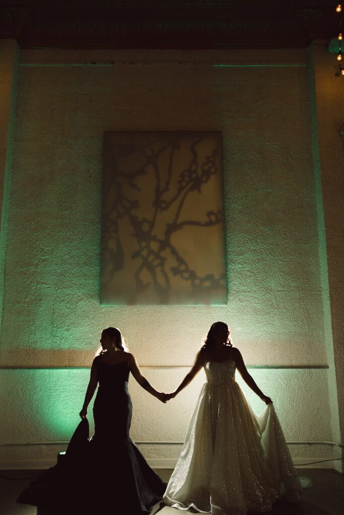 two brides in black and white wedding dresses in front of green and amber uplighting
